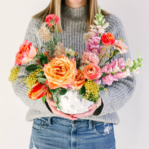large flower arrangement with orange pink and yellow flowers held by girl in gray sweater