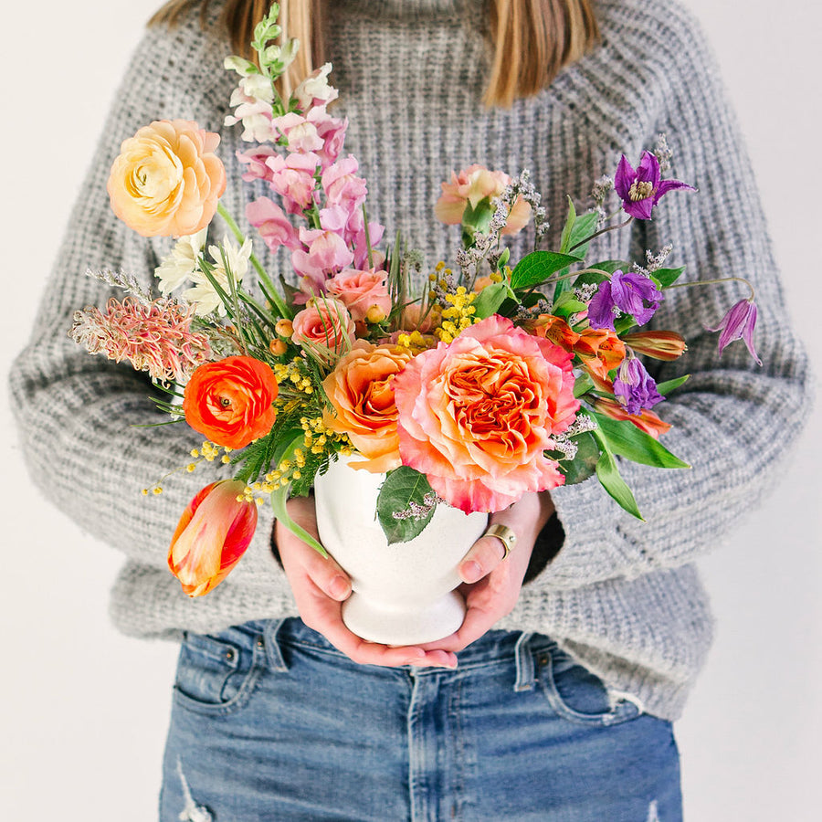 medium flower arrangement with orange pink and yellow flowers held by girl in gray sweater
