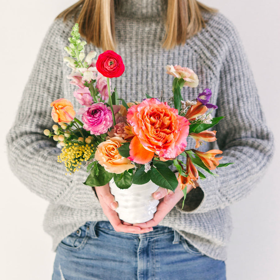 small flower arrangement with orange pink and yellow flowers held by girl in gray sweater