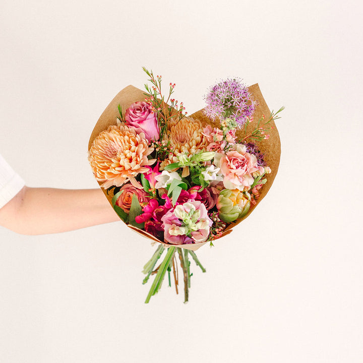 large flower bouquet in outstretched hand with pink orange and purple wildflowers