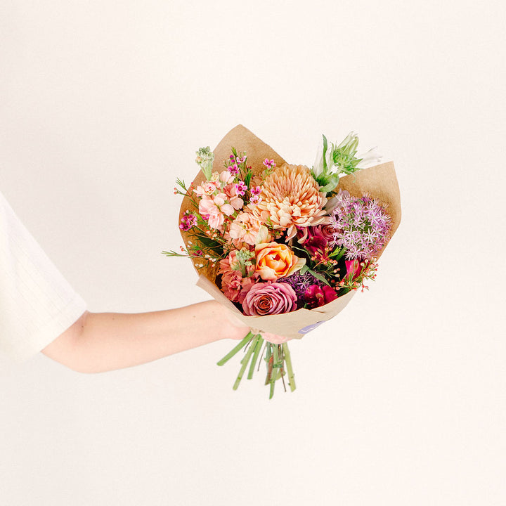 medium flower bouquet in outstretched hand with pink orange and purple wildflowers